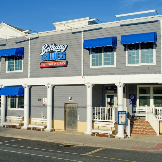 A gray and white two story building with ocean blue awnings on all windows
